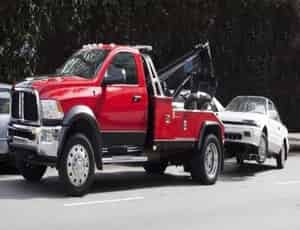 a picture of a red tow truck pulling a white sedan car with a winch 