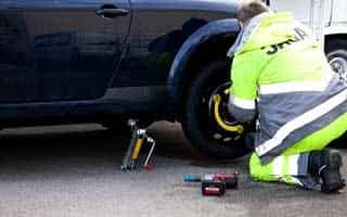 a man in a yellow vest jacket helping to change tires of a car. roadside assistance